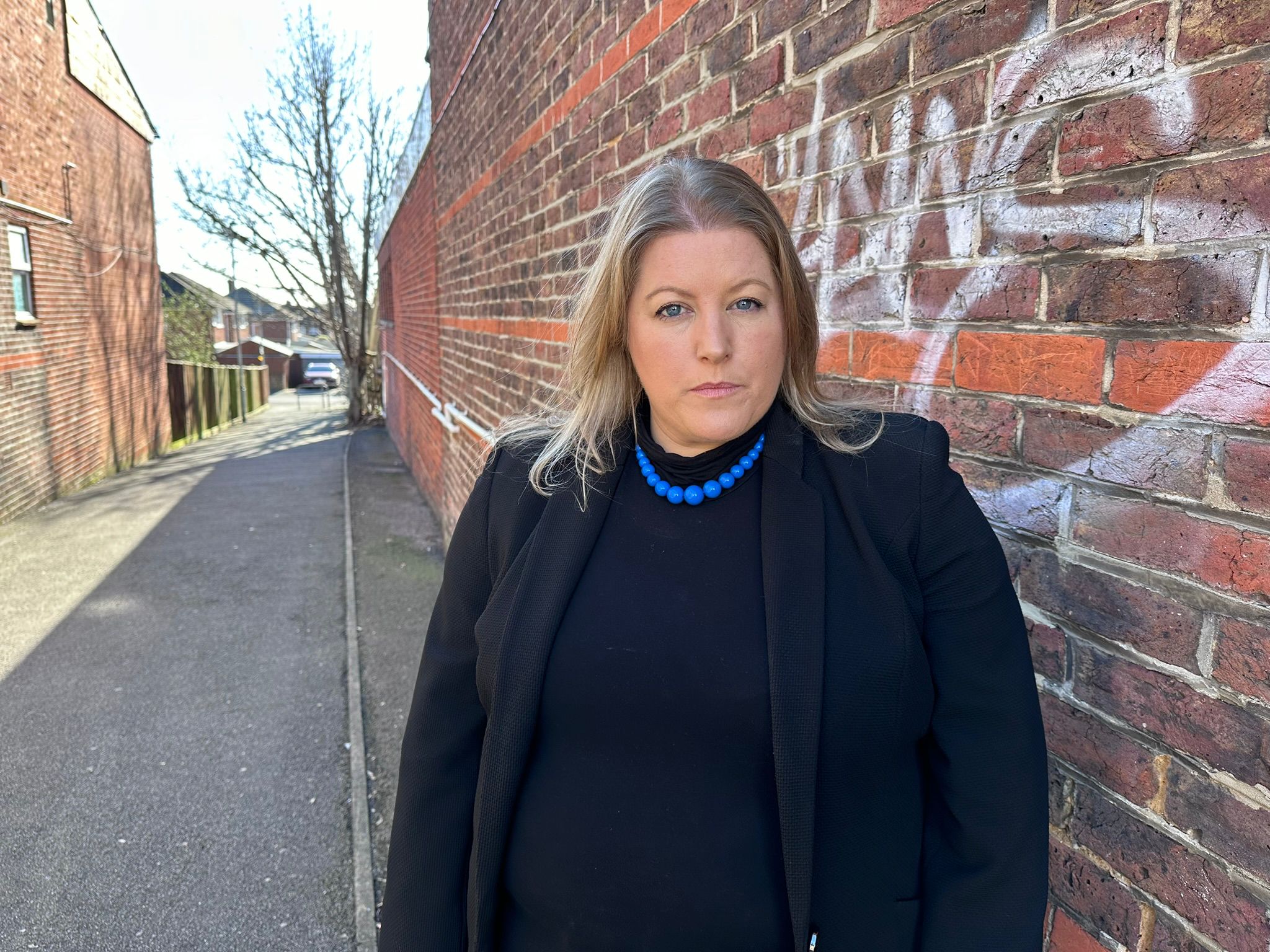 PCC Donna Jones standing next to a graffiti wall wearing black clothing and a blue necklace